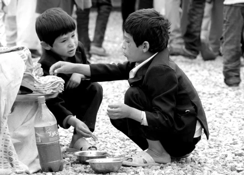 Black and white street photograph of two boys crouched together on the ground